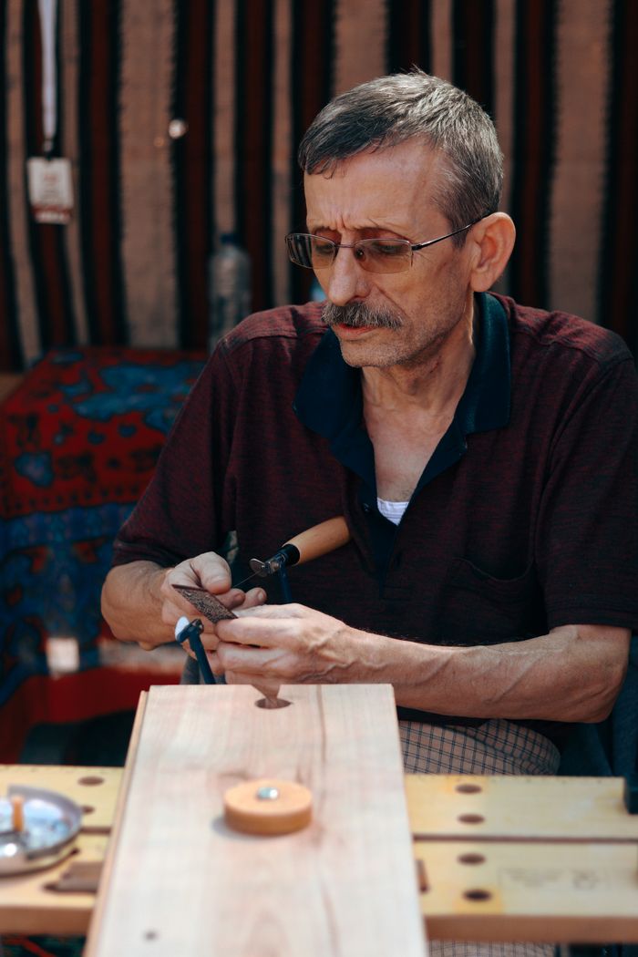 contact-img Elderly man with gray hair focuses on detailed woodworking in a workshop. Portrait of craftsmanship.
