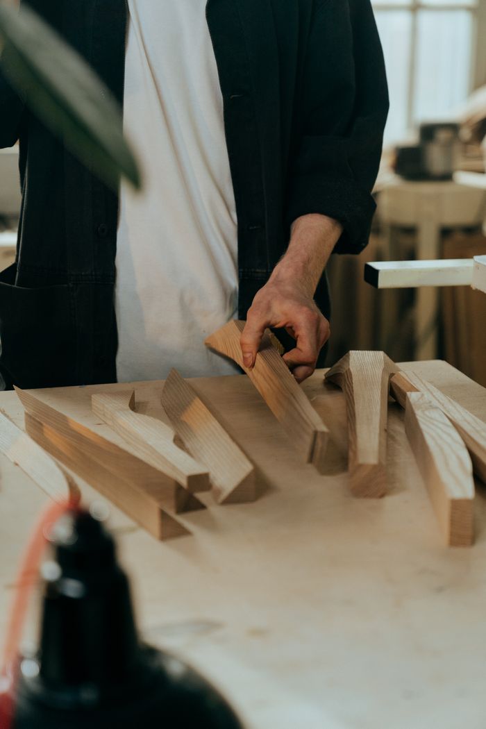 services-03 A craftsman choosing wooden pieces for a project in a sunlit workshop.