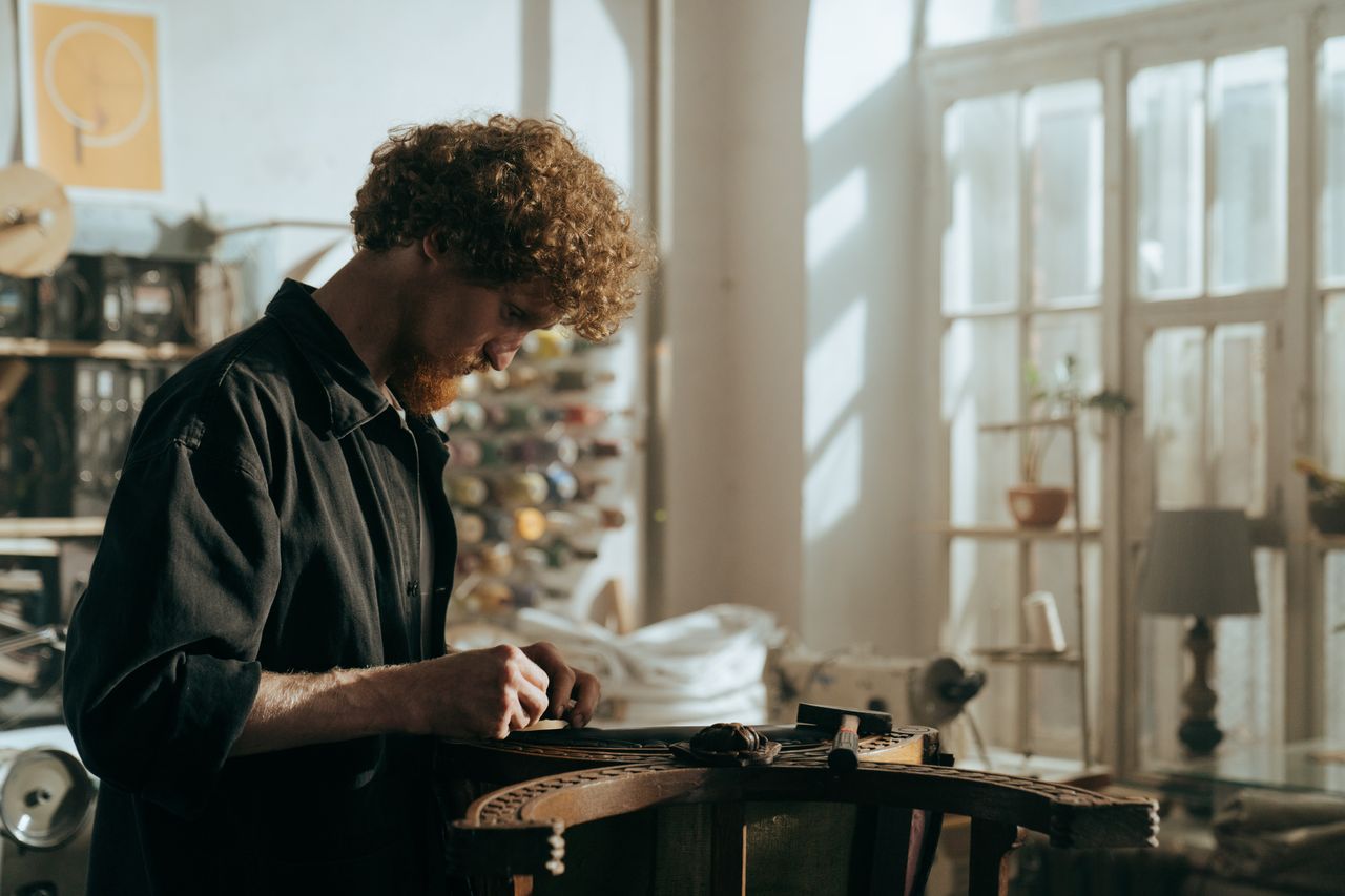 services-01 A redheaded craftsman focuses on restoration work in a sunlit workshop, surrounded by tools and materials.
