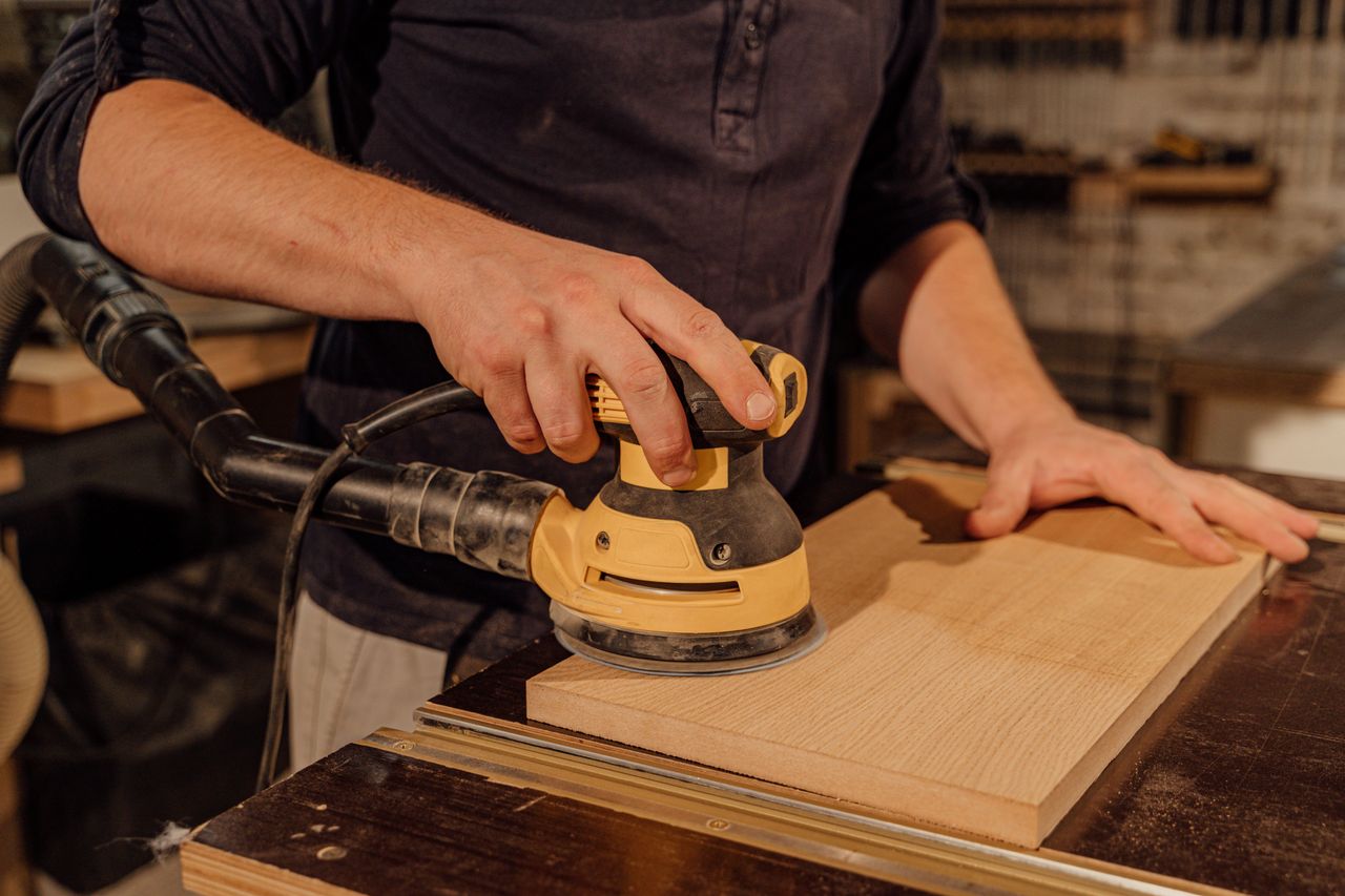 services-02 Carpenter using an electric sander on a wooden board in a workshop, showcasing craftsmanship.
