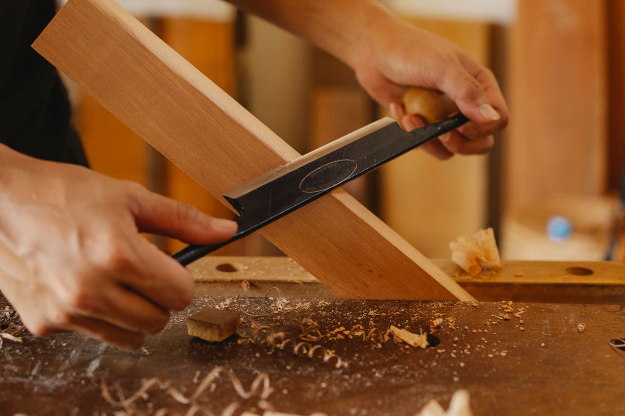 services-02 Faceless joiner cutting hardwood plank with sharp manual tool at workbench in studio