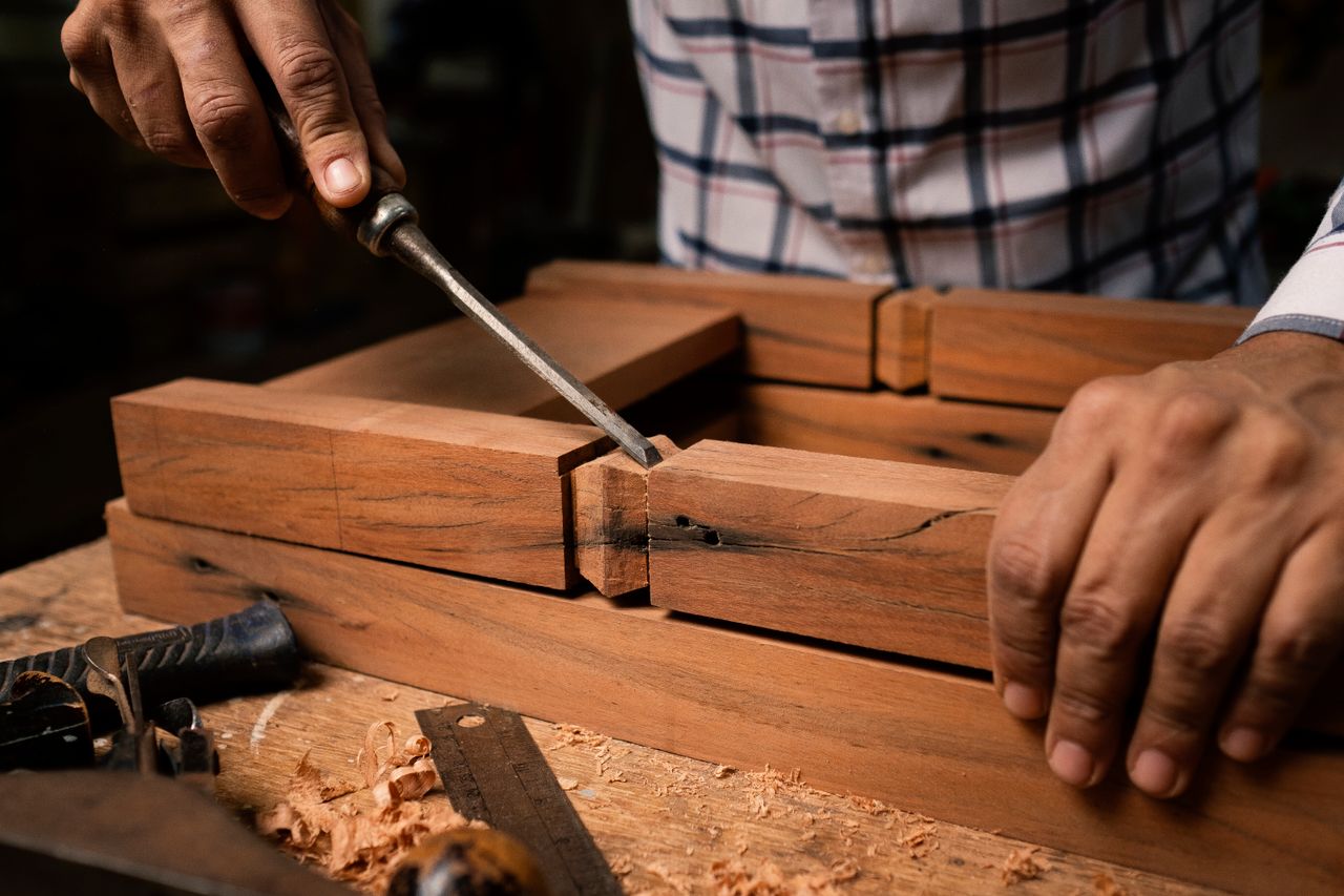 hero-img-02 Focused view of a person skillfully using a chisel on wooden pieces indoors.