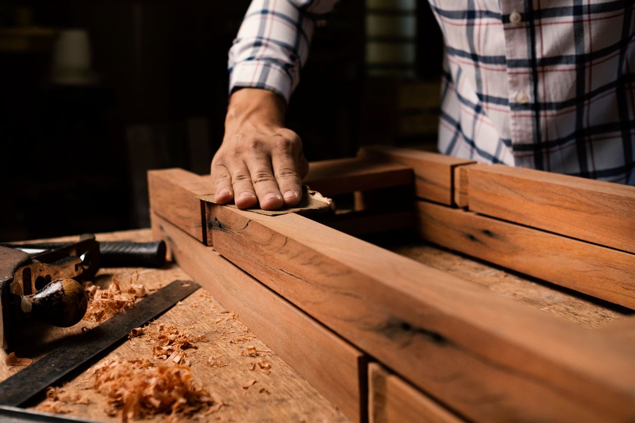 why-choose-us A close-up of a woodworker smoothing a wooden frame by hand in a woodworking shop.
